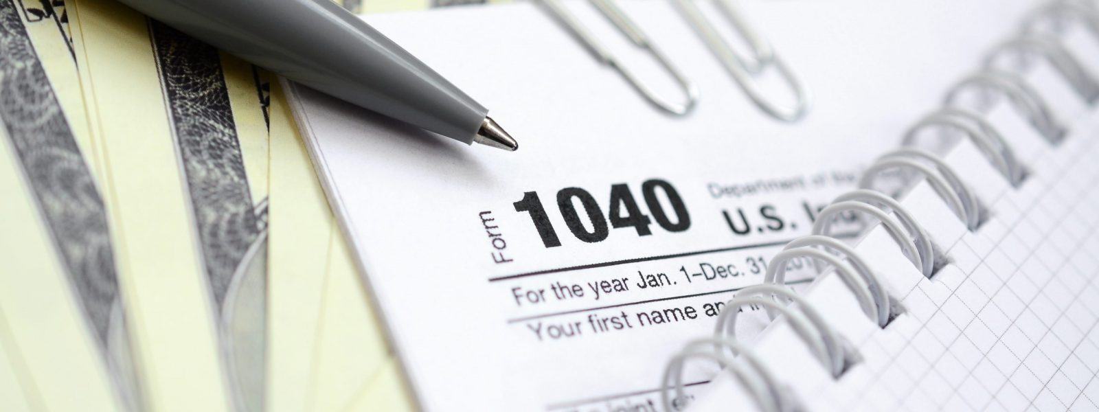 The pen, notebook and dollar bills is lies on the tax form 1040 U.S. Individual Income Tax Return. The time to pay taxes